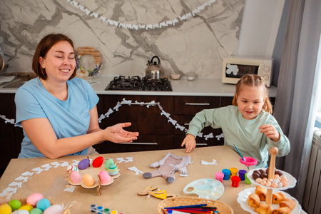 Mid shot of happy Caucasian young mother and her cute little daughter play together at a table with...