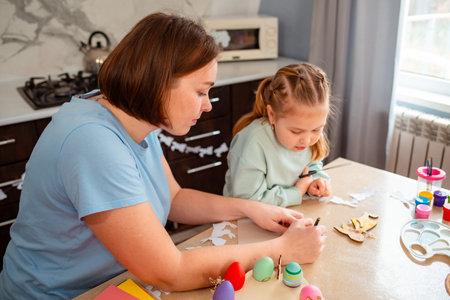 Mid shot of young Caucasian mother and her little daughter carve rabbits out of paper to create...