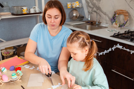 Top view of adult young Caucasian mother and her little daughter cutout rabbits of paper to create...