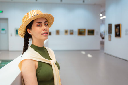 Portrait of young Caucasian elegant woman in straw hat posing in the art gallery. Concept of cultural education for students.の写真素材