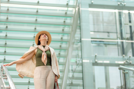 Mid shot of a Caucasian pretty young elegant woman in a straw hat looking up. In the background is a modern business building.の写真素材