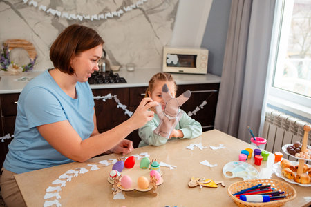 Mid shot of Caucasian happy mother and cute little girl play together with rabbit glove, sitting at...