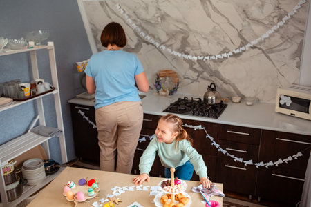 Wide shot of mother and her child playing nearby festive table for Easter. A little girl in a paper...