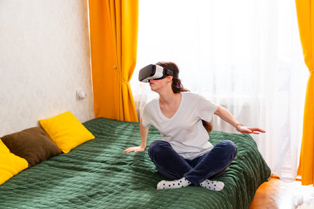Female enjoying advanced technology in a relaxed home setting with VR headset, experiencing limitless possibilities. Mid shot.の写真素材