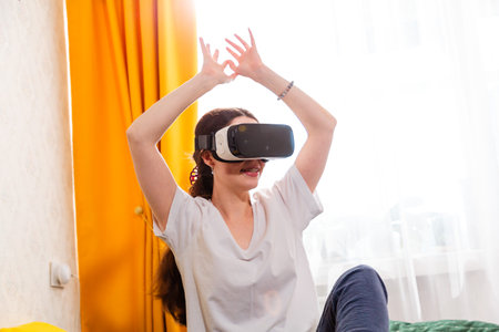 Portrait of woman sitting in stylish bedroom exploring next-generation virtual entertainment with VR headset.の写真素材