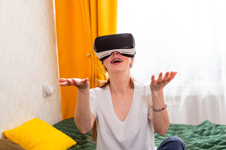 Portrait of young woman sitting in cozy bedroom experiencing high-quality VR gaming, testing next-gen content.の写真素材
