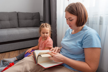 Portrait of young Caucasian woman speech therapist reads a book to a little girl. Teaching...