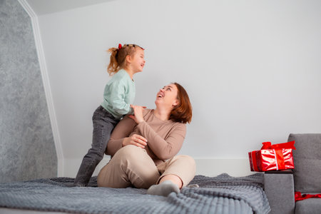 Wide shot of young happy mother and her daughter are playing and having fun together, cuddling on...