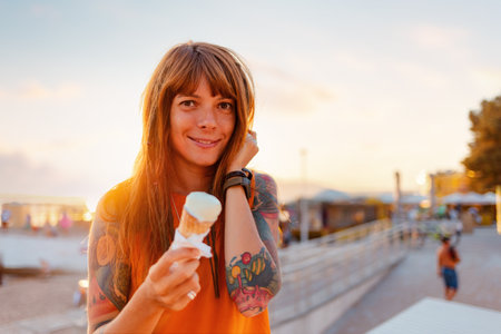 Portrait of young pretty Caucasian woman with tattoos holds ice cream and looking at camera. Copy space. Concept of happiness and summer vacation.の写真素材