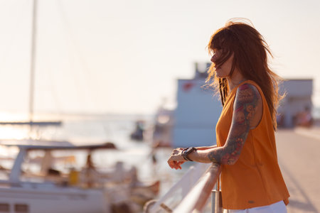 Side view of pretty tanned young woman with tattoos leaning on railing of ship. Copy space. Sea...
