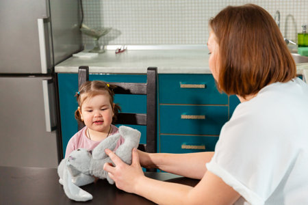 Preschool girl learning and laughing with her mother at kitchen table. Concept of parenting, early childhood development, and educational games at home. Mid shot.の写真素材