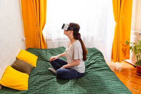 Female embracing interactive VR content while sitting on bed, exploring innovative digital landscapes. Top view, side view.の写真素材