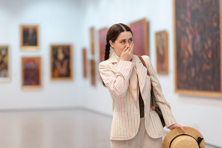 Mid shot a young elegant Caucasian woman experiences embarrassment when visiting a contemporary art exhibition. The concept of the Museum Day.の写真素材