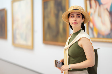 Portrait of a young Caucasian pretty woman in a straw hat and elegant clothes in the gallery of modern art. Copy space. The concept of the Museum Day.の写真素材