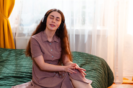 Relaxed girl sitting on the bed, enjoying a musical escape. Mid shot, copy space.の写真素材