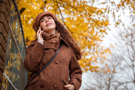 Bottom view of young Caucasian smiling woman with braces on her teeth, wearing a coat and hat call with smartphone standing on the street. Mid shot. Lifestyle and urban life.の写真素材