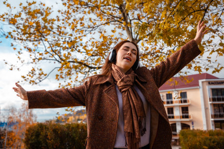 Bottom view of a Caucasian young happy woman in a coat listening to music with headphones in autumn park. Concept of freedom.の写真素材