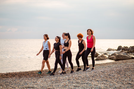 Group of adult Caucasian women walking in row at beach after jogging. Sea and horizon in background. Concept of healthy lifestyle and wellness.の写真素材