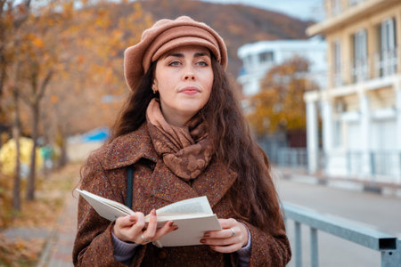 Beautiful Caucasian student in a beret reads in the park during a city walk. Peaceful moment of...