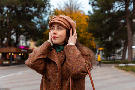 Autumn city walk scene with a young woman in a beige coat and beret listening to her favorite...
