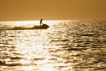 The sea lighted up by a sunset. silhouette of the scooterの写真素材