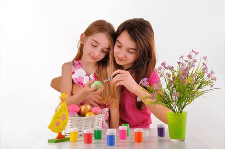  Two girls - sisters painted Easter eggs On the table is a basket with colored eggs, paint for...