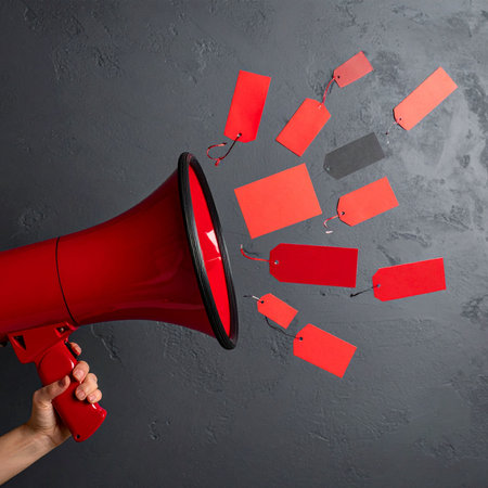 Close up of human hand holding megaphone with blank paper tagsの素材