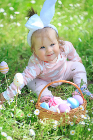 Child searching for eggs in garden. Little girl having fun on Easter egg hunt. Kid in bunny ears and...