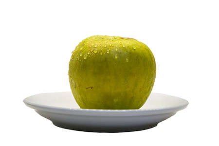ripe yellow-green apple with water drops on a white saucer white backgroundの写真素材