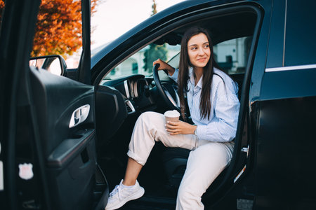 A happy attractive woman or businesswoman holding a cup of coffee and getting out of her modern carの写真素材