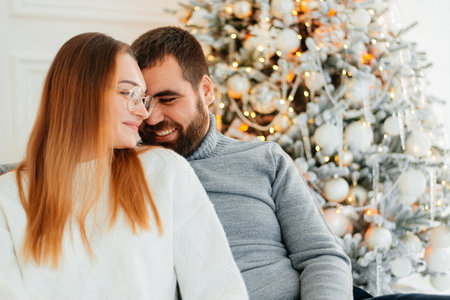 A couple in love hug and kiss near the Christmas tree in the decorated interior of the Christmas tree on a Christmas holiday in winter at home. A man and a woman celebrate the New year together.の写真素材