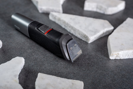 Wireless hair trimmer and beard on gray stone background
