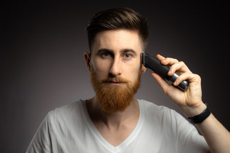 Handsome bearded man cutting his own hair with a clipper