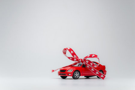 Red model car with bow on a white background. Car as gift, surprise.の写真素材