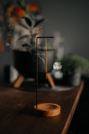 Incense stick smoldering in holder, burning candles, dry flowers on wooden table outdoorsの写真素材