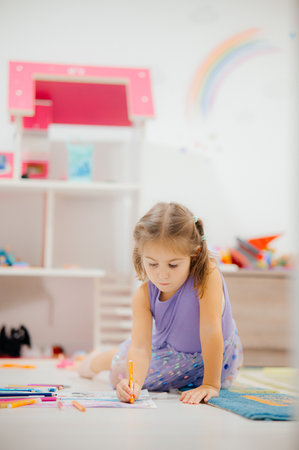 A Creative Child Engaged in Drawing Inside a Playroom Surrounded by Colorful Artworkの写真素材