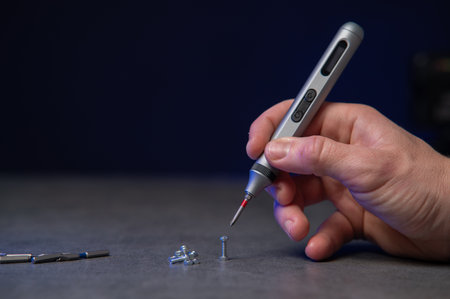 precision electric screwdriver and bits displayed on textured dark surface, product showcase for tool designer, cool blue rim lighting, scattered precisionの写真素材
