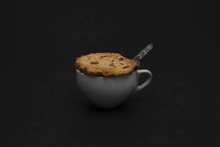 White ceramic cup with homemade biscuit with chocolate pieces and plastic spoon on a black backgroundの写真素材