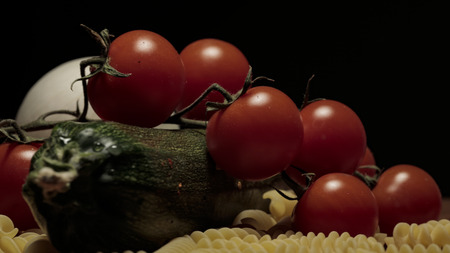 Cherry tomatoes zucchini onion pasta on wooden cutting boardの写真素材