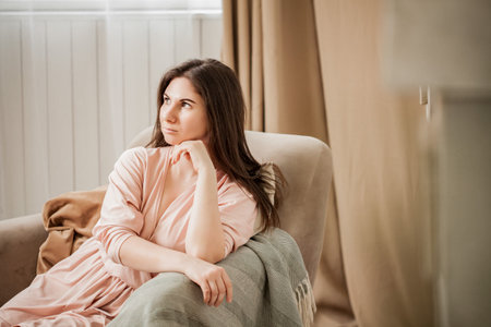 Portrait of a beautiful woman in a bathrobe and beautiful hair sitting in a cozy chairの写真素材