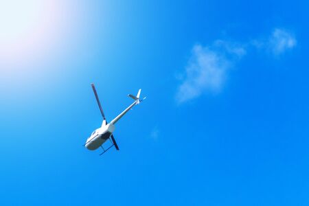 White twin-screw helicopter flies into the distance against the sky and cloudsの写真素材