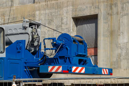 A winch with a metal cable and a hydraulic drive for a construction crane. Blue color. Restriction signs. Automotive base.の写真素材