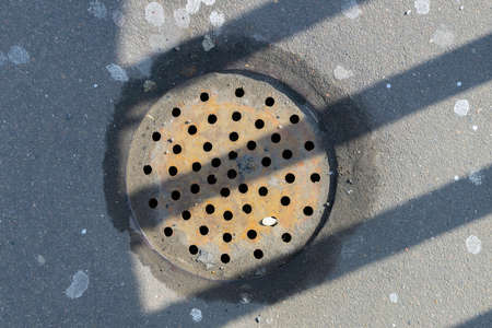 Round storm drain grate with drilled holes in striped shadeの写真素材