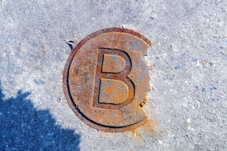 Concept. Bitcoin fell. Decreased demand. A rusty and old metal circle with the letter "b" is partially covered with concrete.の写真素材