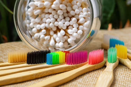 Bamboo toothbrushes with colorful bristles and cotton swabs for cleaning ears in a glass. On the background of green leaves of plants. The concept of unity with nature.の写真素材
