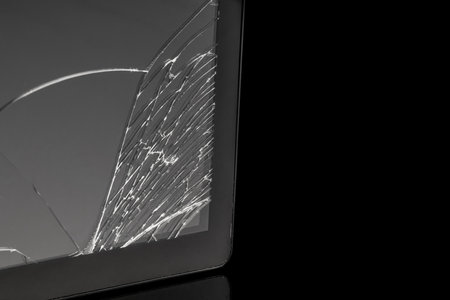 The broken tablet screen covered with many cracks on a dark background with reflectionの写真素材