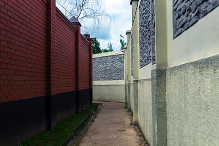 The private construction sector. Passage between two high fences. Brick and stone fences.