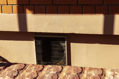 Ventilation outlet closed by grille. Semi-basement. Sharp shadows.