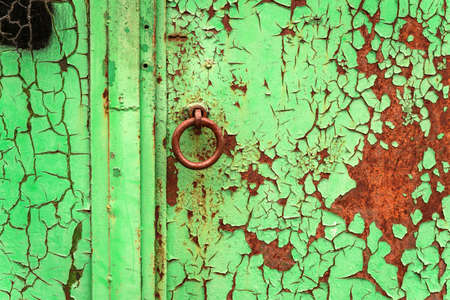 Old metal door with traces of rust and cracked green paint. Round handle made of metal.