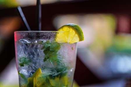 Glass glass with mojito and lime slice. Two straws for drinking. On a blurry background.